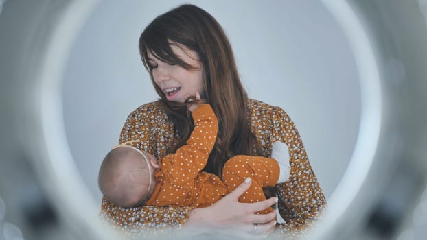 Young mother holding her baby girl, playing and smiling, seen through a ring light reflecting bokeh