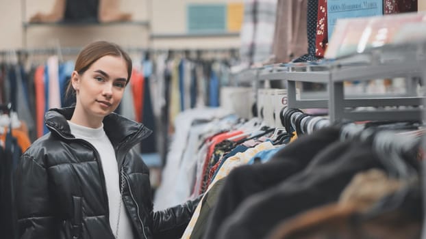 Young customer browsing through clothes on hangers in a thrift store, looking for vintage fashion finds