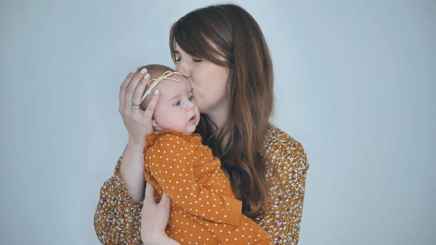 Studio portrait of a happy mother kissing her baby girl on the forehead, holding her in arms, both wearing orange clothes