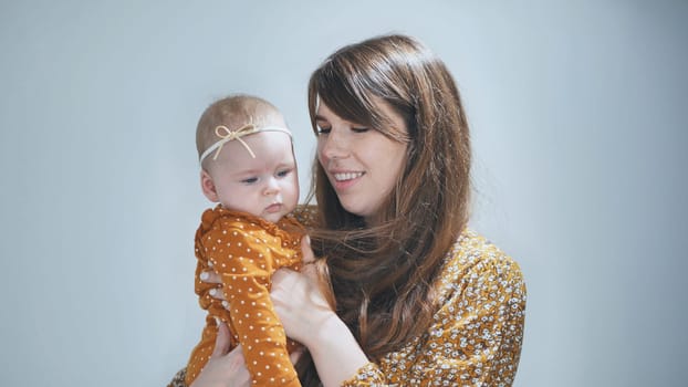 Young mother holding her baby girl, smiling and loving her child, in front of a light blue background