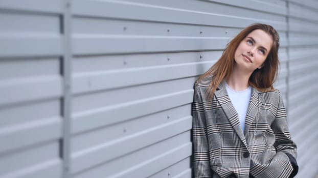 Professional female executive wearing plaid blazer, gazing upward, reflecting near sleek metallic surface with contemplative expression