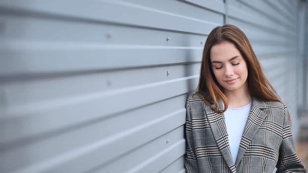 Professional woman resting against metallic wall, wearing checked blazer, experiencing calm moment with closed eyes