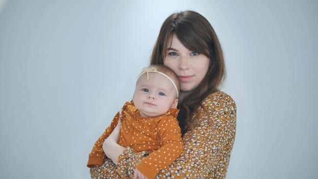 Studio portrait of a loving mother holding her baby daughter, both wearing matching patterned clothes in shades of orange
