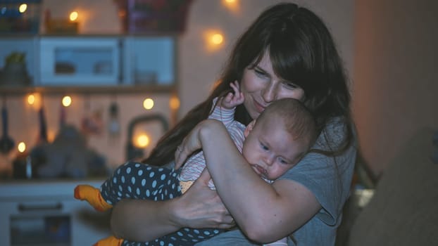 Young mother tenderly embracing her baby in their cozy home, adorned with warm christmas lights, creating a heartwarming scene of love and togetherness