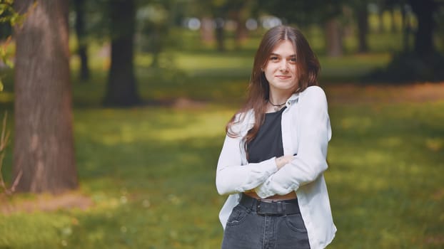 Portrait of a young georgian woman standing with crossed arms in a lush green city park, enjoying the tranquility of nature