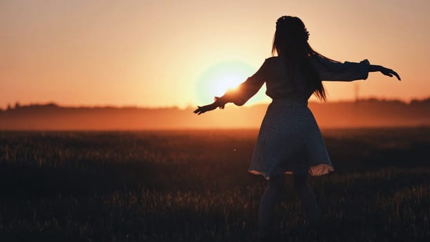 Silhouette of a young woman with open arms enjoying the sunset in a wheat field, expressing freedom and connection with nature