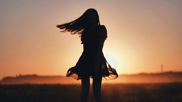 Silhouette of a carefree young woman dancing in a field at sunset, her hair flowing in the wind, expressing freedom, happiness, and connection with nature