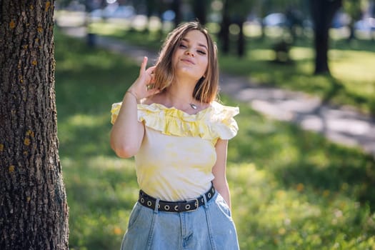 Teenager adjusting her hair while posing confidently near a tree in a park, enjoying the warmth of a sunny summer day