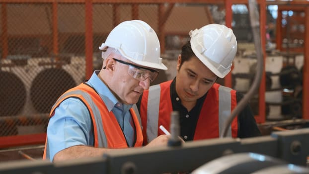 Engineer teaching apprentice to use metal sheet stamping machine, industrial team is working on various projects with tablet computer, worker work together to check the operation system in a factory