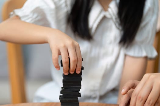 As they play together, a girl focuses on carefully placing a game piece, showcasing teamwork and the joy of shared experiences with family.