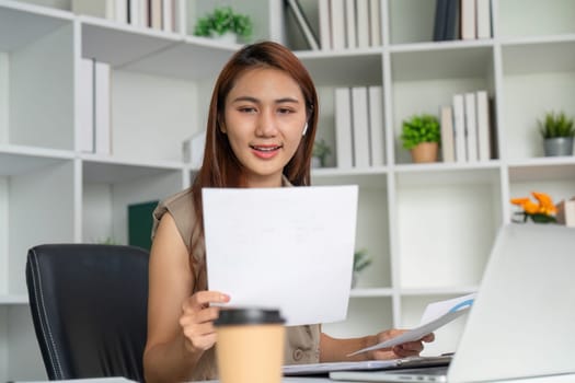 The woman examines important paperwork with focus, reflecting her commitment to productivity in a contemporary workspace filled with plants and organizational elements.
