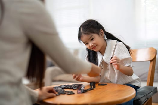 The mother hands a domino to her daughter, sparking joy and creativity in their playtime together, emphasizing family values in a nurturing home.