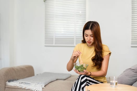 A woman dedicates time to self-care as she enjoys a fresh salad in her cozy living area, demonstrating her commitment to a healthy lifestyle.