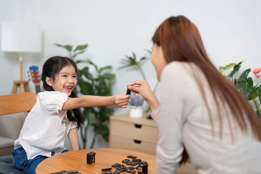 A mother and her daughter enjoy quality time together, engaging in a board game. The girl gleefully hands over a game piece, highlighting their playful interaction and bonding.