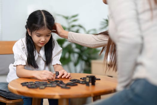 The little girl diligently sorts the game pieces, showing dedication in a playful learning environment while enjoying her mother's company.