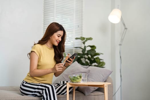 Focused on her wellness, a woman eats a fresh salad and checks her phone, exemplifying modern habits that intertwine health and technology.