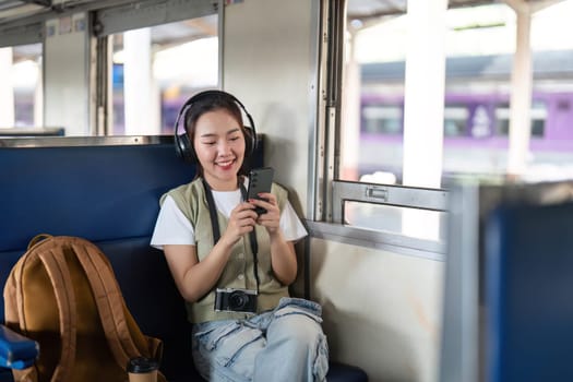 A cheerful traveler in headphones smiles at her phone while enjoying music on a train journey. This image highlights the joy of travel and connectivity.
