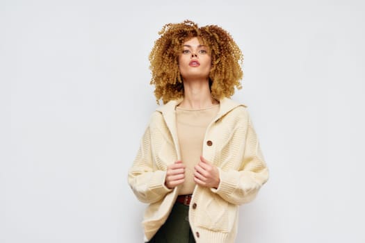 Stylish female model wearing a cream colored oversized sweater and beige top, posing against a minimalistic white background Her curly hair adds a dynamic touch to the chic outfit