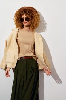 Stylish woman with curly hair dressed in a beige sweater and a green skirt, exuding a confident atmosphere The light background emphasizes her outfit and modern accessories, ideal for fashion focuse