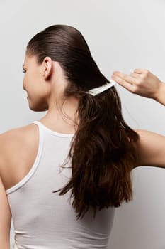 This image features a female model styling her long, healthy hair She is combing her hair gently from the back, showcasing a shiny and smooth texture The background is clean and white, emphasizing the model and her hair care routine