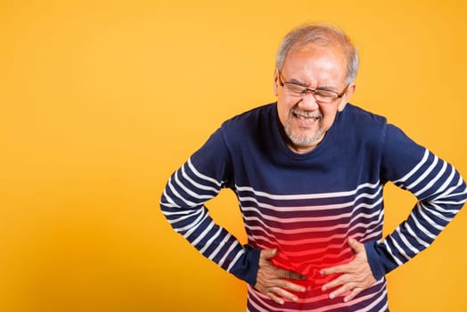 Portrait Asian old man with glasses holds hands on abdomen he stomach ache studio shot isolated yellow background, senior man pensioner feeling pain abdominal pain, hepatitis painful