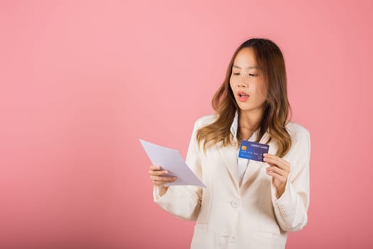 Portrait of Asian young woman holding paper calculating bills on hand and credit card for payment, female person problem she hold worried over bill, studio shot isolated on pink background