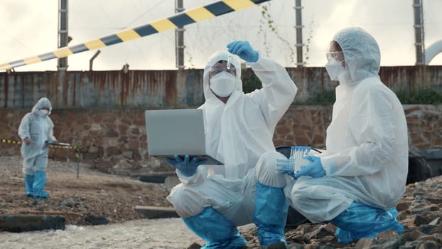 Ecologist sampling water from the river with test tube and save data to laptop computer, Biologist in a protective suit and mask collects sample of waste water from industrial, problem environment