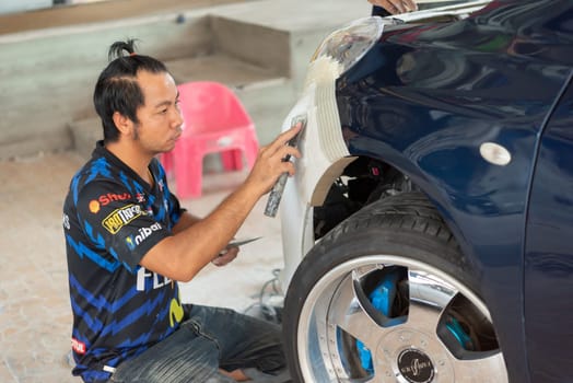 Bangkok, Thailand - April 4, 2024 : Unidentified denter or car mechanic serviceman check and fix body work and fiber bumper body part for fix and repair problem at car garage or repair shop