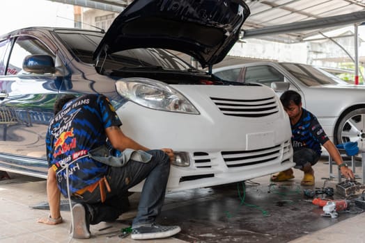 Bangkok, Thailand - April 4, 2024 : Unidentified denter or car mechanic serviceman check and fix body work and fiber bumper body part for fix and repair problem at car garage or repair shop