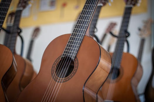 Row of classical acoustic guitars arranged in a music classroom or store. The depth of field highlights one guitar while the others fade into the background, ideal for illustrating music education, instrument selection, or artistic culture.