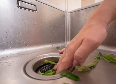 Woman using a garbage disposal to get rid of cucumber peels in a modern sink.