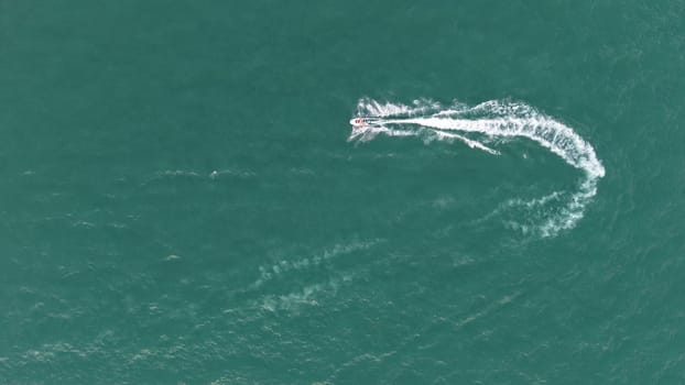 Aerial view of a jet ski creating a white water trail on the turquoise surface of a calm sea, offering a captivating contrast of colors and textures