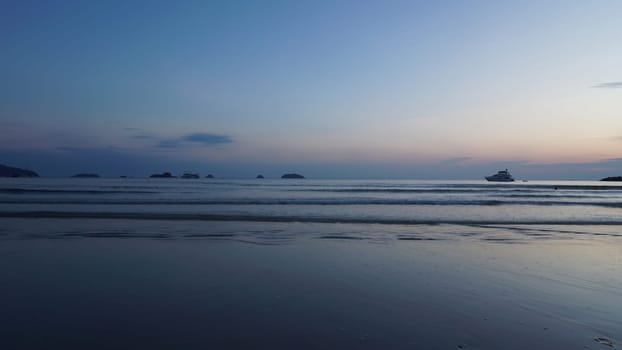 As the sun sets, tourists enjoy the gentle waves of a tropical ocean, with boats dotting the horizon and islands adding a touch of serenity to the tranquil scene
