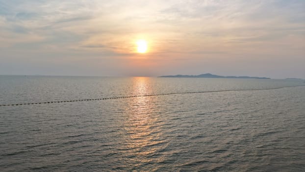 Golden sunlight reflecting on calm ocean waters, with a line of buoys leading towards a distant island beneath a serene pastel sky at dusk, creating a tranquil seascape