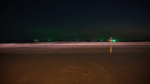 Fishing vessel navigating dark waters, approaching the coast at night, creating a tranquil long exposure seascape with illuminated horizon and smooth waves
