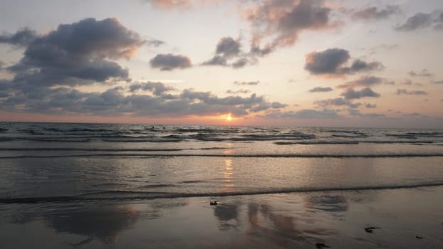 Soft waves gently roll onto the sandy shore as the sun dips below the horizon, painting the sky with vibrant hues of orange and pink during a serene sunset at the beach