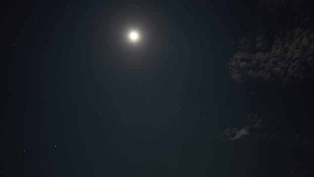 Moon shining brightly in a dark night sky, surrounded by twinkling stars and wispy clouds, creating a tranquil and serene atmosphere of celestial beauty and calmness