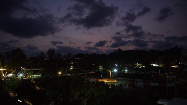 Streetlights casting a warm glow over a deserted water park at dusk, highlighting dramatic clouds and vibrant sunset colors painting the sky, creating a serene evening atmosphere