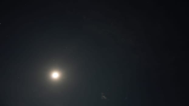 Low angle view of a bright moon illuminating the night sky, surrounded by countless twinkling stars, creating a serene and magical atmosphere