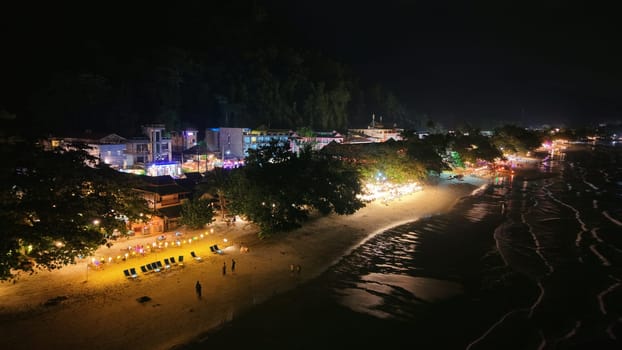 Tourists and vendors mingling at a lively night market on a stunning beach, enjoying a vibrant atmosphere filled with colorful lights and the enticing aroma of street food under the dark sky
