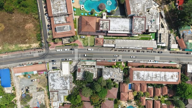 Cars are driving along a road in a tropical resort town, passing by hotels, shops, and a swimming pool, offering a vibrant view of urban life in a vacation destination