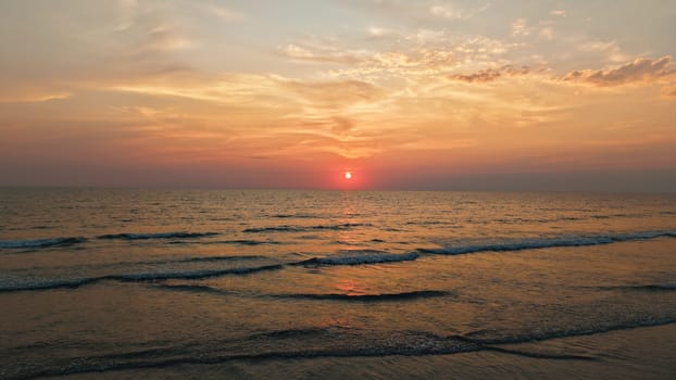 Gentle waves rolling onto the shore during a vibrant sunset, painting the ocean with warm hues of orange and pink, creating a serene and picturesque scene