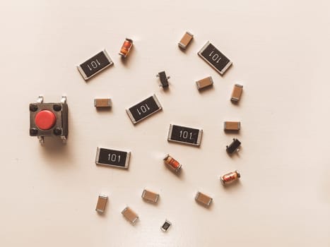 Close-up of various SMD electronic components,diodes, capacitors, and a red tactile push button, arranged on a light background. Ideal for illustrating electronics, DIY tech, and educational materials.