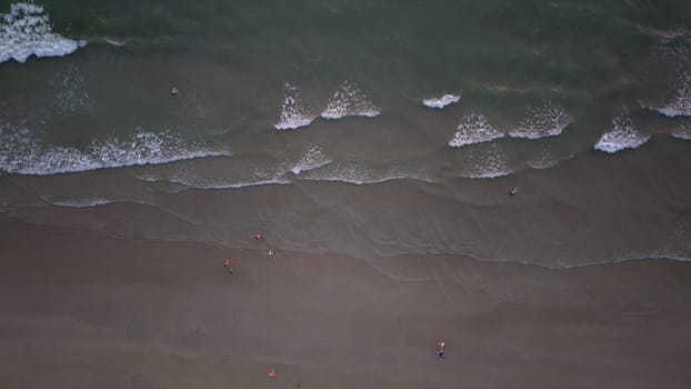 Aerial view of tourists enjoying a relaxing swim in the ocean waves on a beautiful sandy beach, creating a serene and idyllic vacation scene