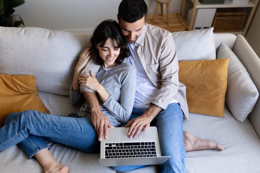 High angle view of happy couple using laptop relaxing sitting on the sofa at home. Lifestyle and technology.