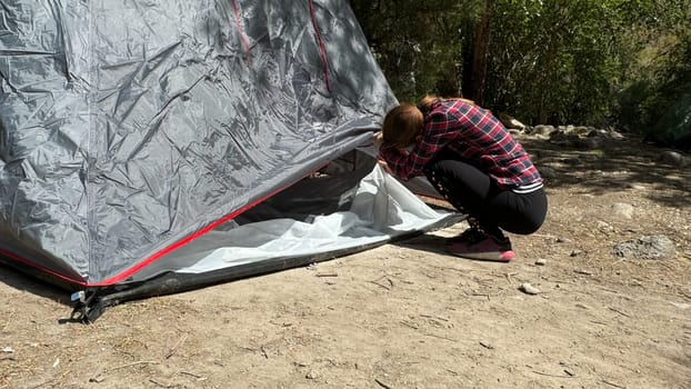 Young woman assembling a tent in a scenic mountain landscape during summer. Outdoor camping activity with clear space for text