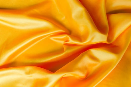 Macro shot of golden silk cloth draped in gentle folds with a polished satin finish