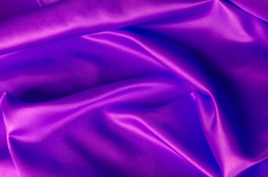 Top view of shiny maroon satin cloth with radiant surface highlights and fine woven texture in natural folds.