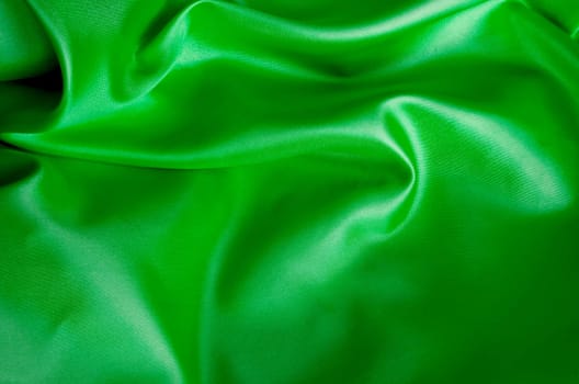 Silky satin fabric in vibrant green with elegant creases and shine. Suitable for design and wallpaper background.