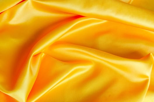 Shiny yellow satin cloth with radiant surface highlights and fine woven texture in natural folds.